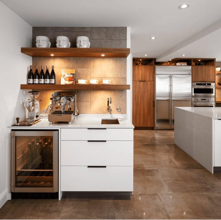 Modern small-space coffee bar with white cabinetry, built-in wine fridge, espresso machine, wood floating shelves, warm under-shelf lighting, and neutral tile backsplash in a contemporary kitchen.