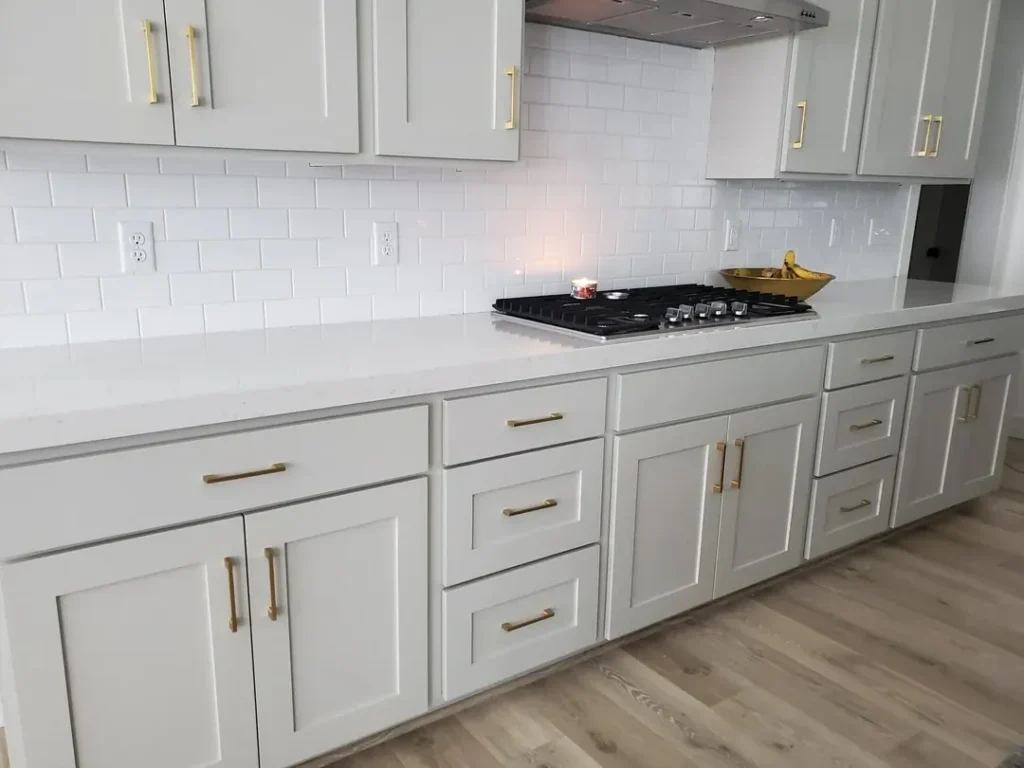Modern kitchen with white shaker cabinets, white subway tile backsplash, white quartz countertop, and gold cabinet handles.