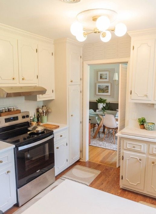 Warm cream kitchen with white cabinets, stainless steel stove, wood floors, and soft lighting in a cozy traditional home interior.