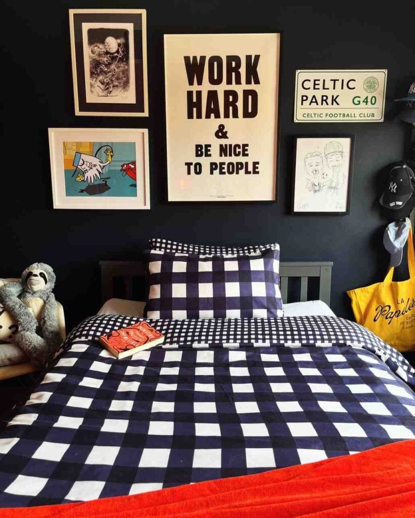 Navy and white gingham bedding in a young boy's bedroom with a dark accent wall, gallery-style framed artwork, motivational typography print, sports signs, wall-mounted caps, and colorful accessories creating a modern, personalized space.