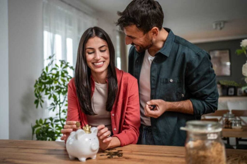 Smiling couple adding coins to a piggy bank at home while working together to save money and manage their finances.