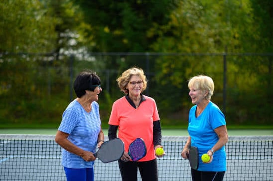 Three senior women enjoying a game of pickleball together on an outdoor court.
