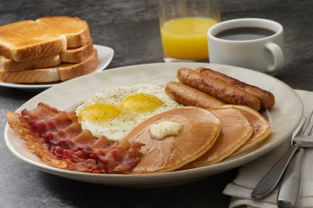 Grand Slam Breakfast with Pancakes, Bacon, Sausages Sunny Side up Eggs and Toast