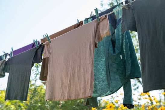 T-shirts and other clothing hang from a clothesline with clothespins, drying outdoors in the sunshine.
