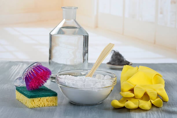 Baking soda, vinegar, rubber gloves, a sponge, and a scrub brush arranged together for inexpensive homemade cleaning.
