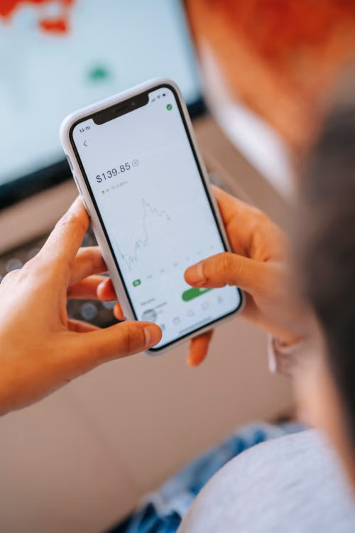 A person holds a smartphone displaying a financial app with a balance and market chart on the screen.