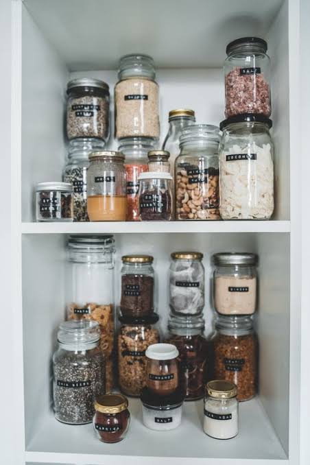 Glass jars filled with grains, beans, seeds, pasta, and other dry goods are neatly arranged on pantry shelves.