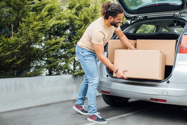 Man loading cardboard moving boxes into the open trunk of a car.