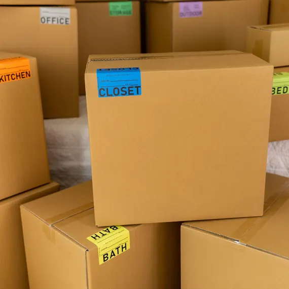 Stacked cardboard moving boxes labeled by room, including closet, kitchen, office, and bath.
