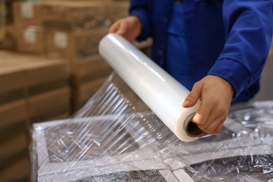 Person wrapping furniture with a roll of clear plastic stretch wrap.