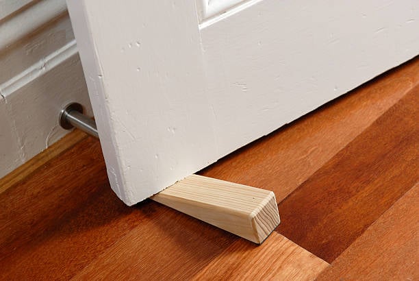 Wooden doorstop holding a white door open on a hardwood floor.