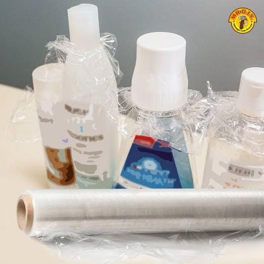 Several toiletry bottles with plastic wrap secured around their openings, with a roll of plastic wrap in front.