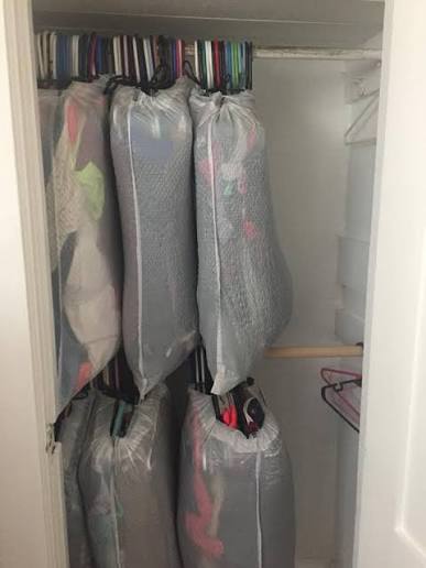 Clothes hanging in a closet with large protective bags pulled up around groups of garments.