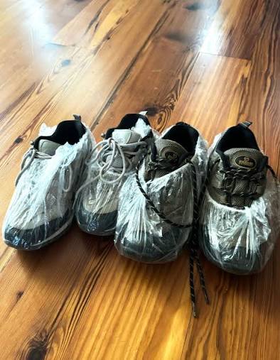 Four pairs of shoes on a wooden floor, with each pair wrapped in clear plastic bags to keep them clean during packing.