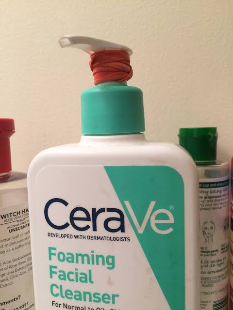Bottle of CeraVe foaming facial cleanser with a rubber band wrapped around the pump to prevent it from dispensing during travel or moving.