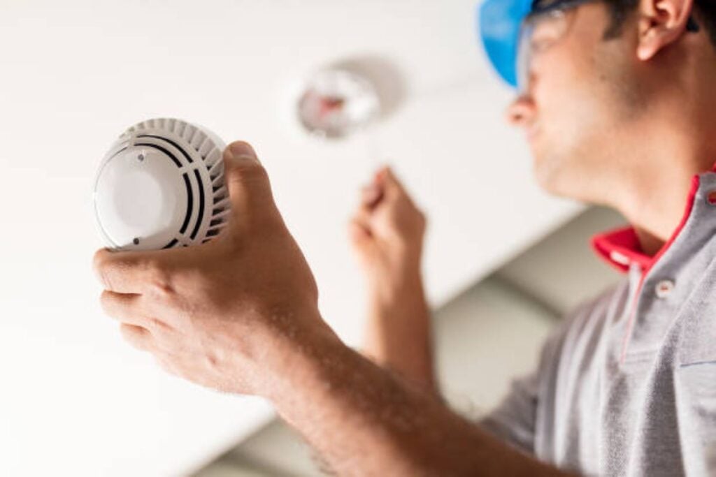 Technician installing or replacing a smoke detector on the ceiling of a home.