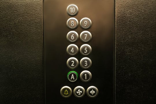Close-up of an elevator control panel with numbered floor buttons and the “A” button illuminated green.