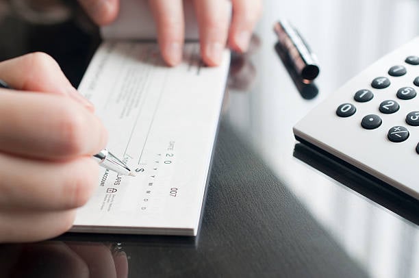 lose-up of a person filling out a paper check beside a calculator on a desk.