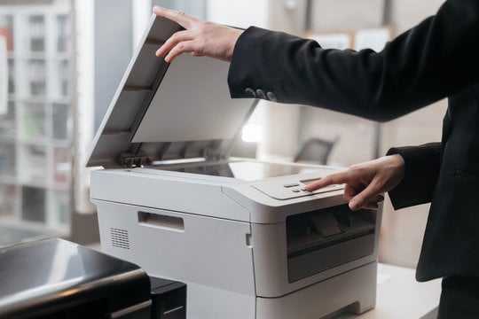 Person using a large office printer and scanner with the lid raised.