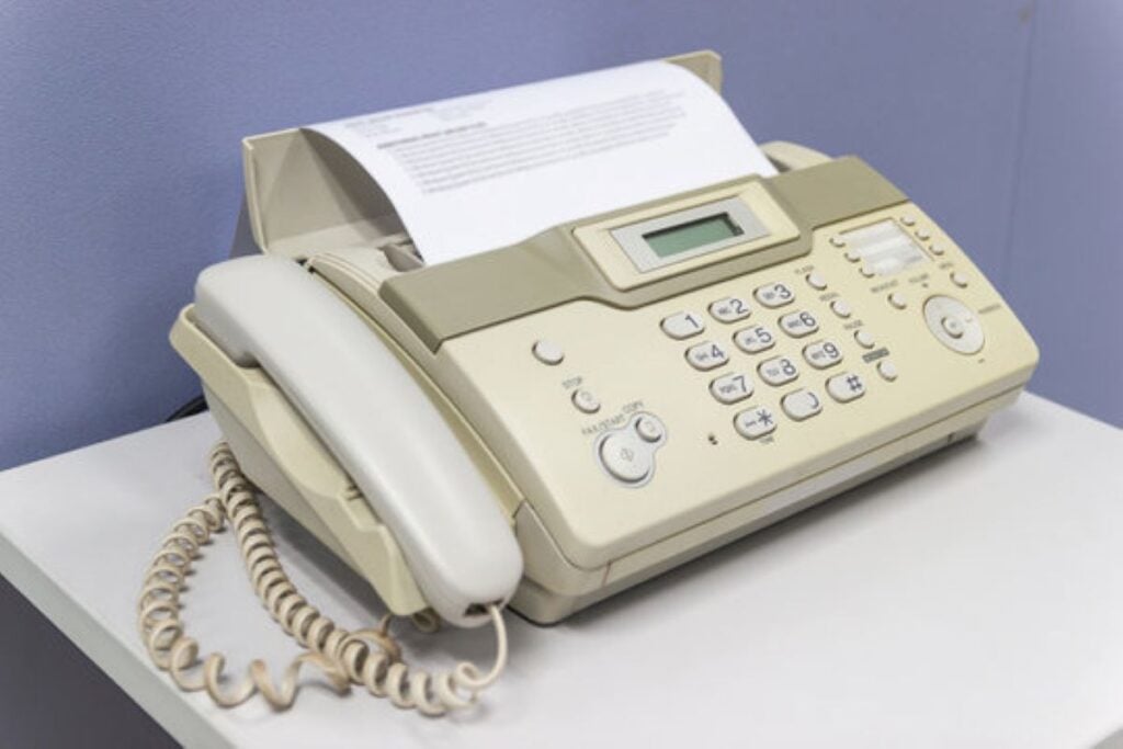 Beige fax machine with a corded telephone handset and a sheet of paper loaded on top.