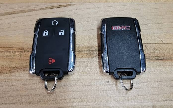 Two black GMC car key fobs lying side by side on a wooden surface.