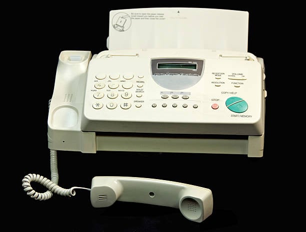 Older beige fax machine with a telephone handset, keypad, display screen, and paper tray.