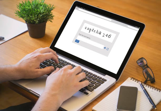 Person typing on a laptop displaying a CAPTCHA verification code on the screen.