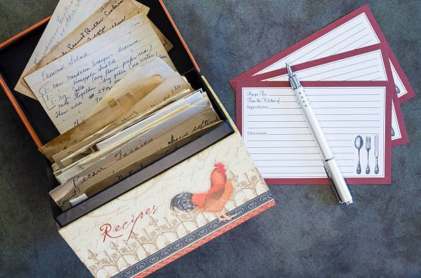 Recipe box holding vintage recipes along with blank recipe cards on deep green textured background