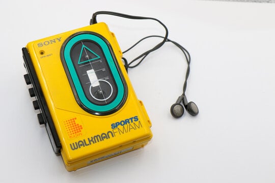 Yellow vintage Sony Sports Walkman cassette player with black earbuds on a white background.